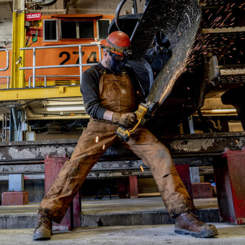 Skilled worker angle grinding metal while wearing Carhartt Workwear for protection. Get your hands on durable and reliable workwear from Carhartt, available at McCaskie.store. Visit our website today!